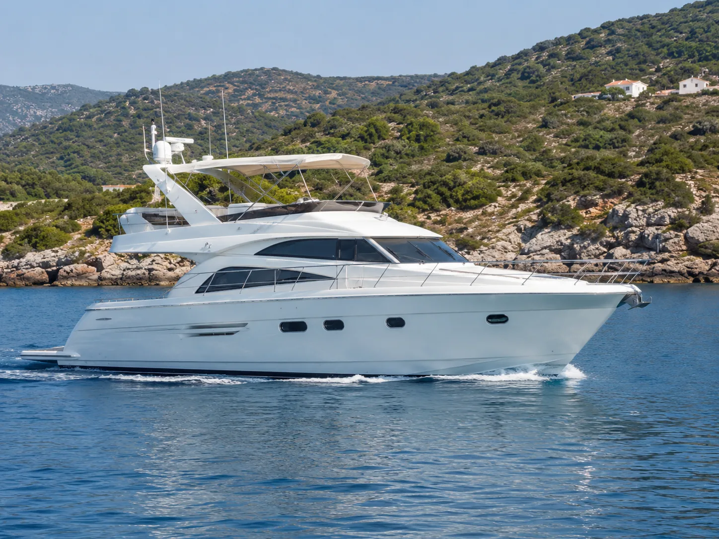 White flybridge motor yacht cruising along a rocky Greek coastline